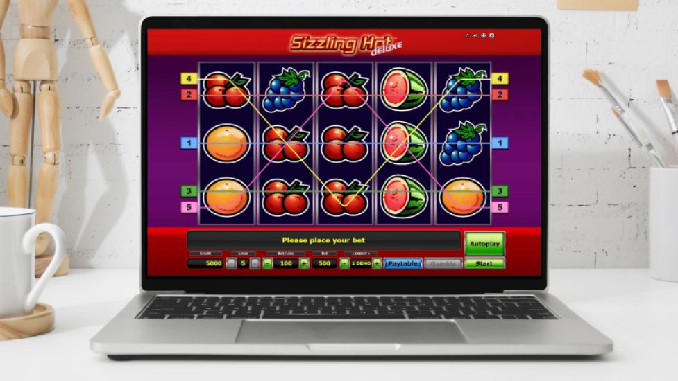 Laptop pokazujący slot Sizzling Hot Deluxe z tradycyjnym motywem owoców i 5 liniami wypłat.